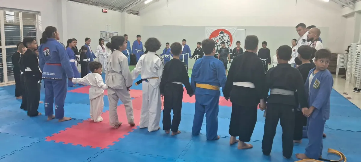 Crianças e professores de mãos dadas em roda no tatame